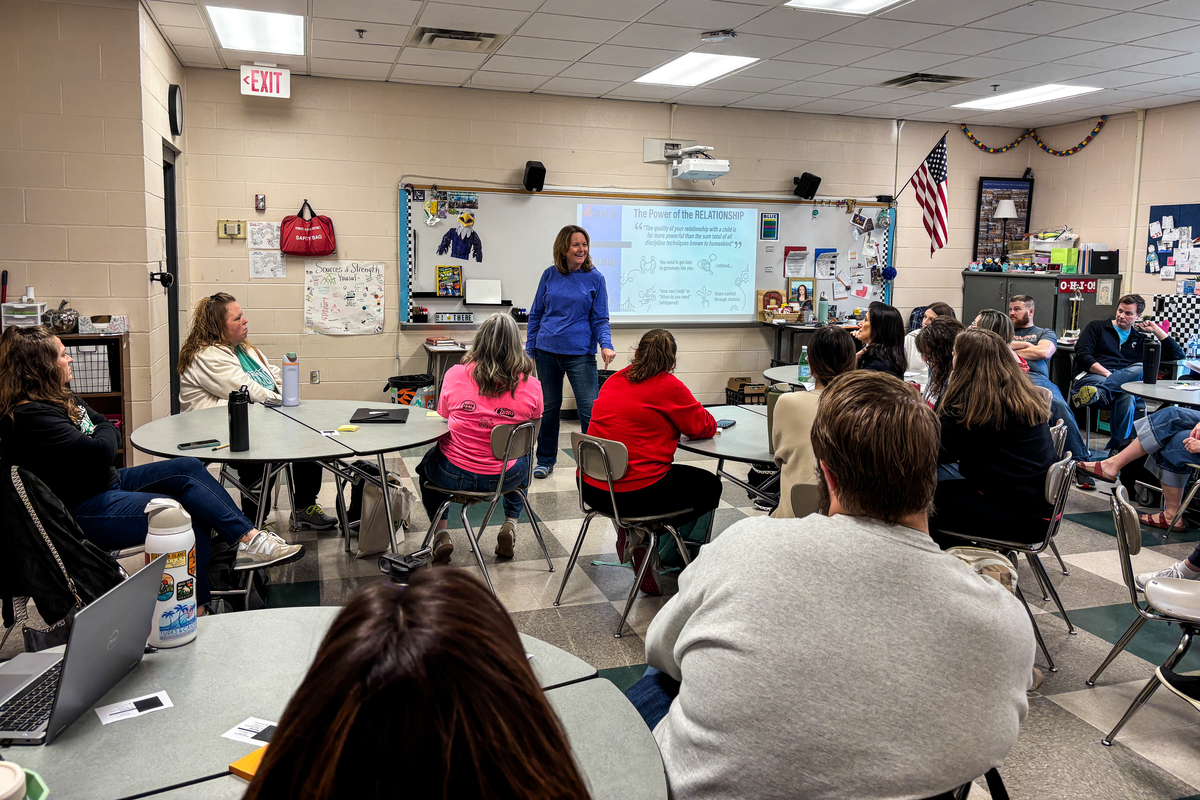 A teacher in a blue sweatshirt presents to colleagues